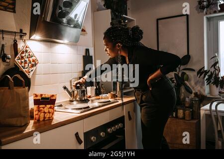 Giovane donna che fa il tè in cucina a casa Foto Stock