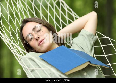 Donna rilassata che dorme sull'amaca con un libro sul petto in una foresta Foto Stock