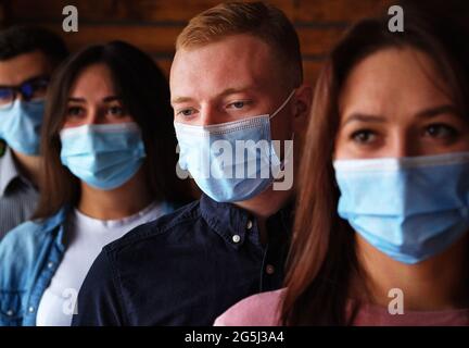 Un gruppo di giovani che indossano maschere durante la pandemia del covid-19 - una folla di persone tristi che indossano maschere contro il coronavirus - uomini e donne che indossano m Foto Stock