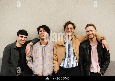 Ritratto di felici amici maschi multietnici contro il muro beige Foto Stock