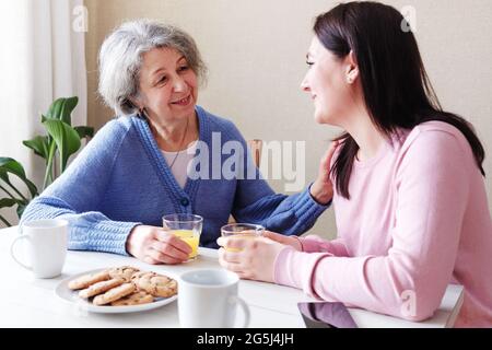 Una figlia visita una madre anziana e parlano insieme a colazione - UNA donna in pensione è visitata da un volontario e parla per mantenere l'healt mentale Foto Stock