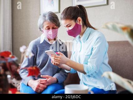 Una figlia adulta visita una madre anziana e trascorre del tempo con lei nel soggiorno sul divano - UN volontario ha visitato una donna anziana e aiuta t Foto Stock