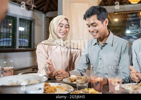 un uomo e una donna che indossano i copricapo ridono mentre prendono i piatti laterali quando rompono il digiuno insieme Foto Stock