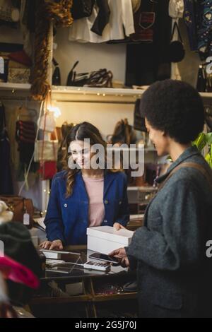 Cliente femminile che paga tramite smartphone al momento del check-out al proprietario in boutique Foto Stock