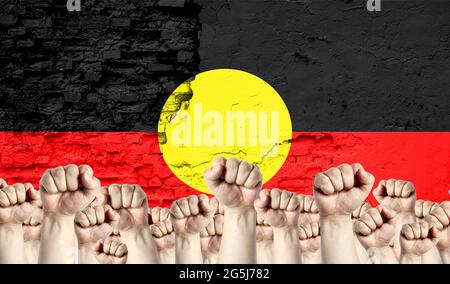 Innalzato pugni di uomini sullo sfondo della bandiera dell'Aborigeno Australiano dipinto sul muro, il concetto di unità popolare e l'opinione di t Foto Stock
