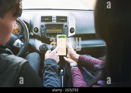 Un paio di giovani guidano in auto - un uomo e una donna guardano un navigatore che si muove in auto - un navigatore in un'auto che cerca una strada Foto Stock