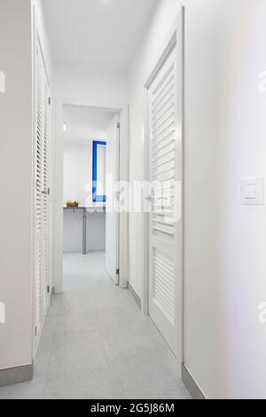 Corridoio interno di colore bianco con porte a sarda in legno. Verticale Foto Stock