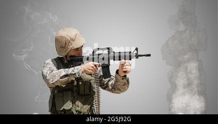 Composizione di un soldato maschio che tiene la pistola, contro parete di cemento con fumo e fiamme Foto Stock