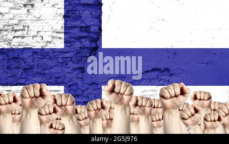 Innalzato pugni di uomini sullo sfondo della bandiera della Finlandia dipinta sul muro, il concetto di unità popolare e l'opinione della maggioranza. Foto Stock