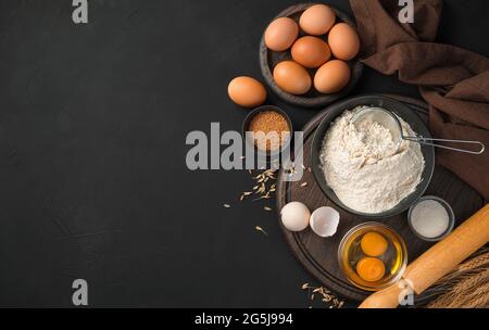 Ingredienti per cucinare piatti di farina. Farina, uova, zucchero su fondo nero. Foto Stock
