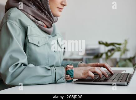Vista laterale ritagliata ritratto della moderna donna medio-orientale che indossa un foulard in ufficio e che utilizza un computer portatile, spazio per la copia Foto Stock