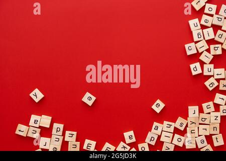 Immagine di sfondo le lettere sono sparse in disordine. Lettere inglesi. Lettere quadrate di legno su sfondo rosso brillante. Biglietto d'auguri, pronto all'uso Foto Stock