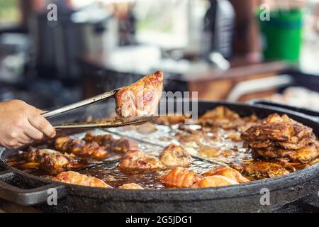 Tenere a mano un pezzo di carne prelevato da una padella grande in pinze da cucina. Foto Stock