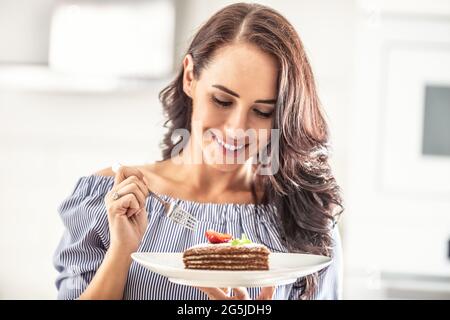 Torta marrone e bianca a strati con foglie di fragola e menta sulla parte superiore tenuta da una donna con una forchetta. Foto Stock