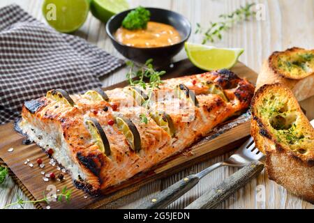 Filetto di salmone succoso con fette di lime su una tavola di legno di cedro alla griglia fresca dal grill del bollitore Foto Stock