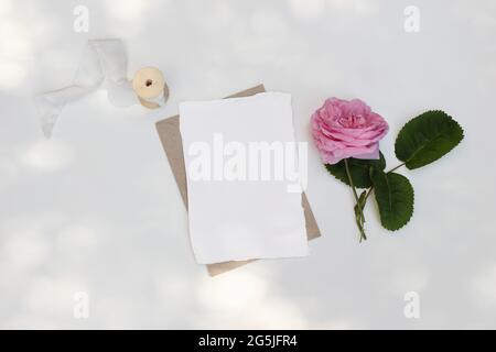 Mock-up di cancelleria per matrimoni estivi. Biglietto d'auguri vuoto, invito con busta artigianale su tavola bianca alla luce del sole. Rosa rosa, rosa Foto Stock