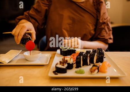 Le mani da donna in primo piano versano la salsa di soia per il sushi. Persona irriconoscibile al bar Foto Stock