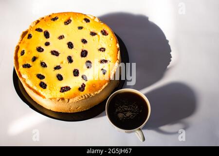 Grande torta di formaggio fresca su piatto nero e tazza di caffè da vicino, con finestra su sfondo bianco. Foto Stock