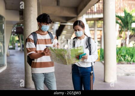 Viaggi, uomo e donna stanno leggendo carta mappa. Indossando maschera, portare zaini e bagagli. Maglietta spogliata e occhiali. Foto Stock