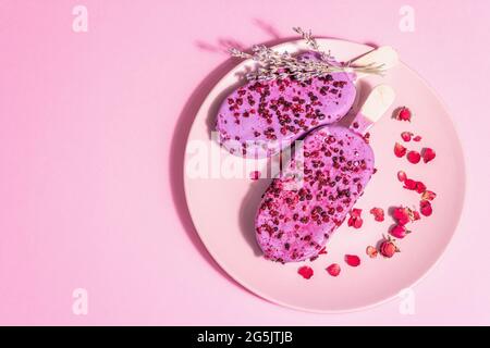 Gelato ai petali di lavanda e rosa, dolce freddo. Luce dura alla moda, ombra scura. Sfondo rosa pastello, vista dall'alto Foto Stock