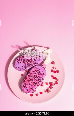 Gelato ai petali di lavanda e rosa, dolce freddo. Luce dura alla moda, ombra scura. Sfondo rosa pastello, vista dall'alto Foto Stock