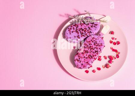 Gelato ai petali di lavanda e rosa, dolce freddo. Luce dura alla moda, ombra scura. Sfondo rosa pastello, vista dall'alto Foto Stock