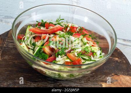 Insalata vegetariana fresca in recipiente di vetro su vecchio tavolo in legno compensato sullo sfondo di una parete di mattoni imbiancati Foto Stock