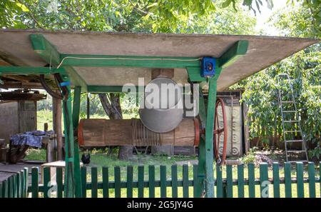 Un pozzo d'acqua vecchio con un secchio nel giardino, un manico di metallo per sollevare l'acqua dal suolo. Villaggio ben sotto il tetto con una corda. Retro bene io Foto Stock