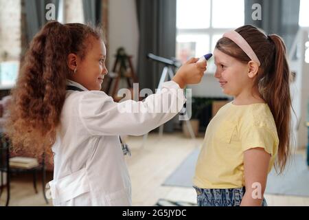 Una delle due bambine che misura la temperatura mentre gioca il medico Foto Stock