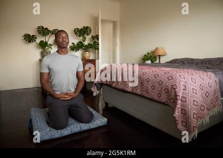 Giovane africano meditando sul pavimento della sua camera da letto Foto Stock