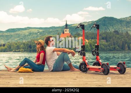 Giovane coppia che usa lo scooter elettrico come moderno mezzo di trasporto ecologico mentre esplora il verde paese Slovenia in vacanza. Energia ecologica verde Foto Stock