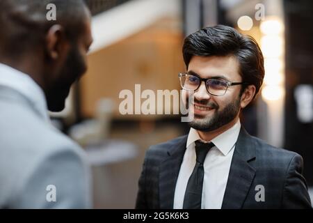 Ritratto di sorridente uomo d'affari mediorientale che parla con il compagno mentre si trova nella hall dell'hotel Foto Stock