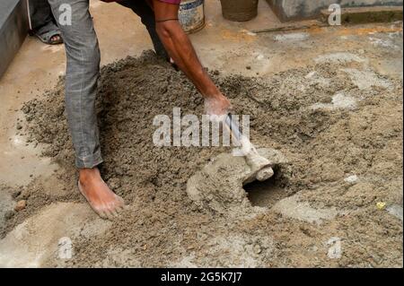 Kolkata, Bengala Occidentale, India - 6th Gennaio 2020 : lavoro indiano che mescola cemento ed acqua manualmente sul pavimento usando una pala. Immagine stock. Foto Stock