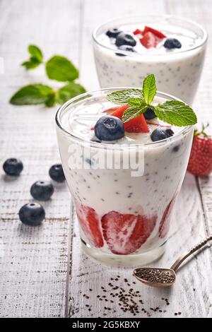 Due semi di cia di fragola frullato a strati o frullato di latte con fragola e menta di mirtillo in vetro su sfondo grigio chiaro. Estate e dieti sani Foto Stock