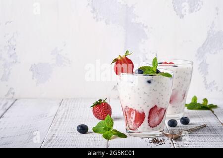 Due semi di cia di fragola frullato a strati o frullato di latte con fragola e menta di mirtillo in vetro su sfondo grigio chiaro. Estate e dieti sani Foto Stock