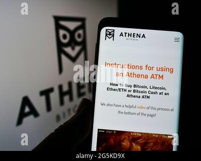 Persona che tiene il cellulare con pagina web della società americana di criptovaluta Athena Bitcoin sullo schermo davanti al logo. Mettere a fuoco il centro del display del telefono. Foto Stock