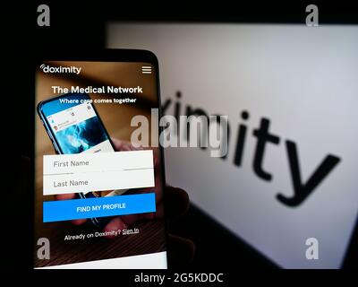 Persona che tiene il telefono mobile con il sito web della piattaforma di rete medica statunitense Doximity Inc sullo schermo davanti al logo. Mettere a fuoco il centro del display del telefono. Foto Stock