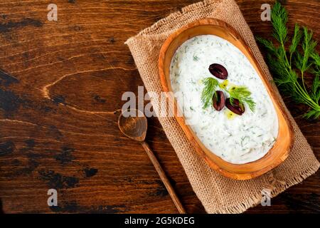 Salsa tradizionale greca o tuffo Tzatziki, yogurt, cetriolo, aneto, aglio e olio di sale in rustico recipiente di legno su sfondo di legno. Stile rustico. Selez Foto Stock