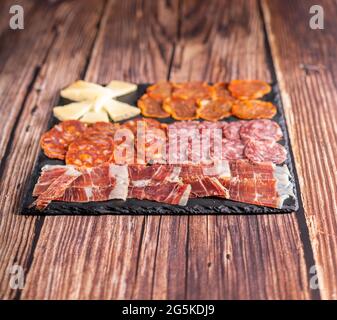 Fotografia gastronomica di chorizo, salame, prosciutto, formaggio e altri antipasti su una tavola scura. Tipico pasto di tapas spagnole su un tavolo di legno. Foto Stock