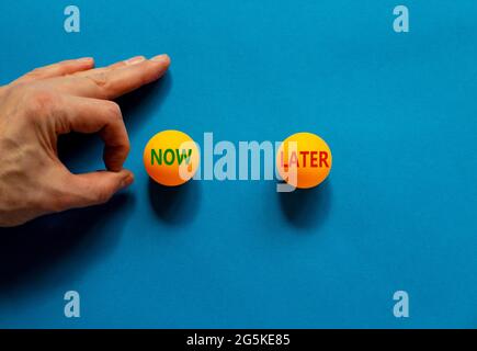 Simbolo ora o successivo. La mano maschio sta per far scorrere la palla. Palline da ping-pong arancione con le parole ora più tardi. Splendido sfondo blu. Affari, ora o. Foto Stock