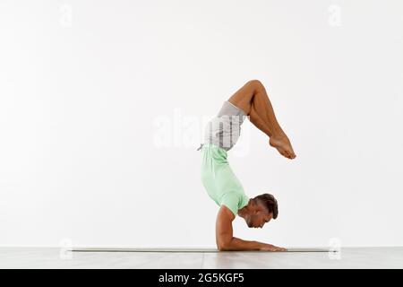 Sporty giovane uomo facendo backbend handstand, yoga, pilates, allenamento fitness in piedi in equilibrio mento asana Foto Stock