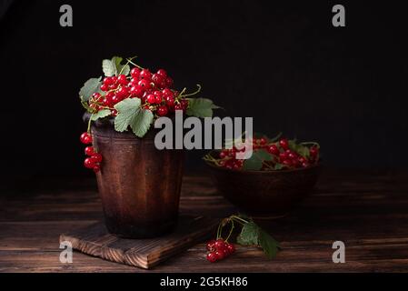 Bacche di ribes rosso mature in una ciotola di argilla su sfondo scuro, frutti di bosco estivi, primo piano. Foto Stock