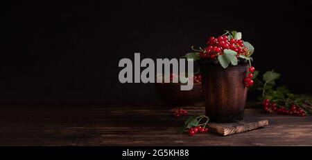 Bacche estive, bacche di ribes rosso mature in una ciotola di argilla su sfondo scuro, striscione, primo piano. Foto Stock