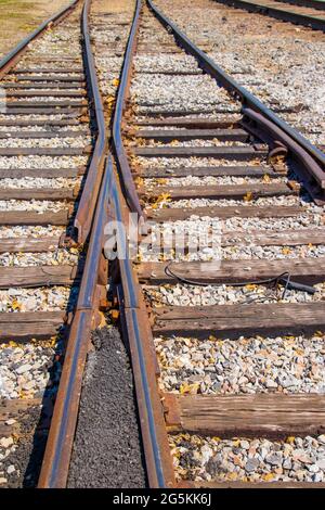 La fusione dei cingoli - due vecchie linee ferroviarie arrugginite si uniscono con alcune foglie di caduta sparse tra la ghiaia - fuoco selettivo Foto Stock