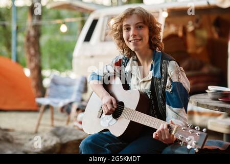 Ritratto di giovane donna che sorride alla macchina fotografica mentre suona la chitarra sulla natura Foto Stock