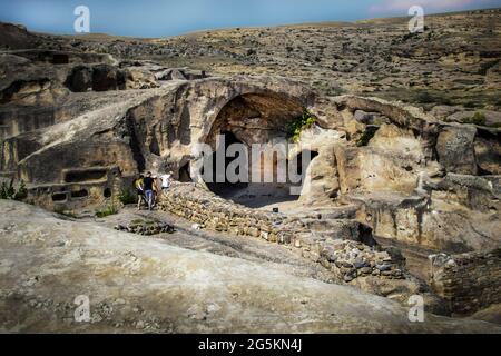 Due coppie giovani fanno la loro strada giù per esplorare un Profonda grotta scura nella preistorica Uplistsikhe Cave Town vicino a Gori Georgia Foto Stock