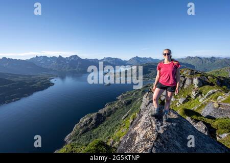 Giovane escursionista in piedi su rocce, Fjord Raftsund e montagne, vista dalla cima di Dronningsvarden o Stortinden, Vesterålen, Norvegia, Europa Foto Stock