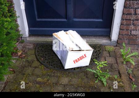 Scatola di cartone di consegna danneggiata sulla porta anteriore di una casa, confezione fragile con ammaccature, concetto di consegna errato Foto Stock