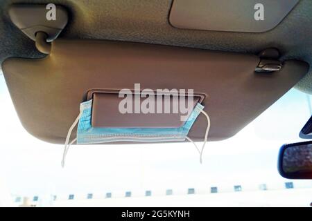 Maschera medica sotto la visiera in un'auto durante un viaggio Foto Stock