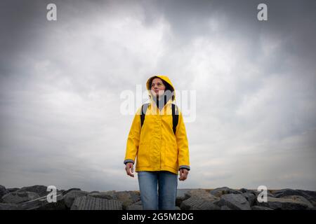 Donna escursionista che indossa un cappotto giallo in piedi su rocce in tempo cattivo. Foto Stock